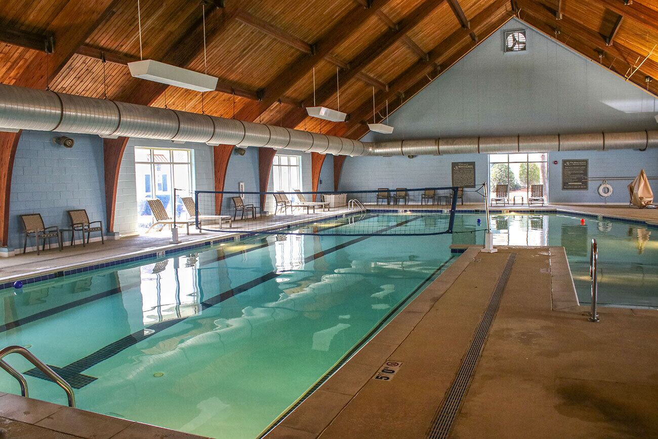 Une piscine intérieure avec un plafond haut, une zone de baignade claire et des chaises longues.