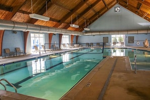 Une piscine intérieure avec un plafond haut, une zone de baignade claire et des chaises longues.