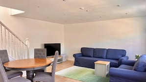 Una sala de estar con una mesa redonda de madera, sillas tapizadas en gris, un sofá azul y una mesita auxiliar.