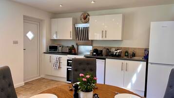 A modern kitchen with white cabinets, a microwave, a stove, and a sink. There is a dining table with plates and a flower vase.