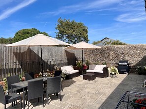 An outdoor patio with wicker furniture, two umbrellas, a barbecue grill, and a stone wall. - Selden Lodge (Worthing)