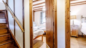 Una escalera de madera que conduce a un dormitorio con una cama, un mesita de noche y una lámpara.