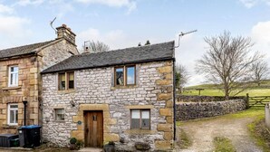 Una casa de piedra con puerta de madera, un pequeño porche y un camino de entrada de grava.