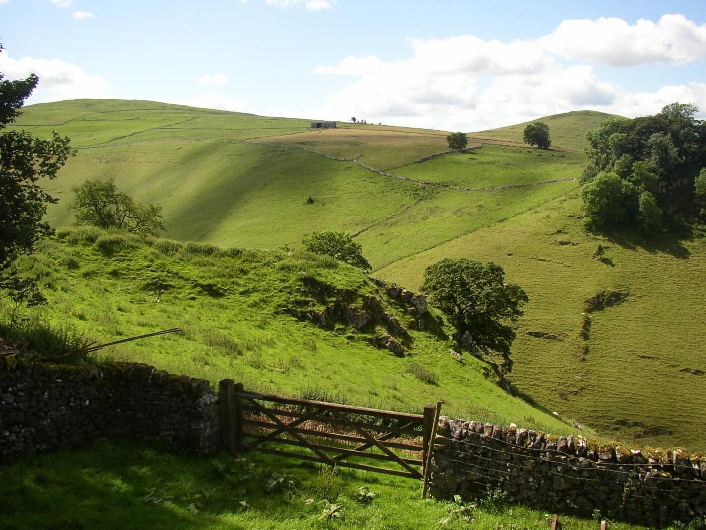 Des collines verdoyantes et ondulées, un mur de pierres et un portail en bois.
