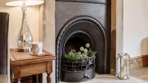 Une cheminée surmontée d’une arche en métal, une table avec une lampe et une plante décorative.