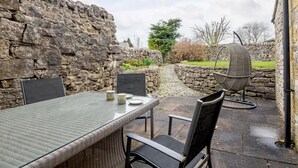 Un mur en pierre, une table d’extérieur avec des chaises et un fauteuil suspendu.