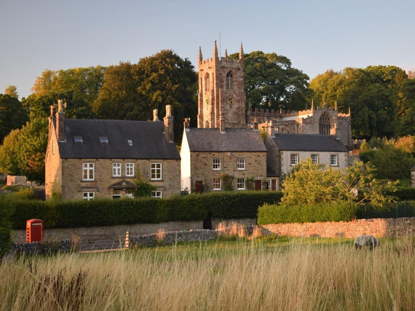 A historic building with a prominent tower, surrounded by traditional stone houses and lush greenery.