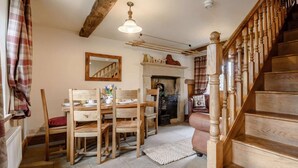 Une table à manger en bois avec des chaises, une cheminée, un miroir et un escalier.