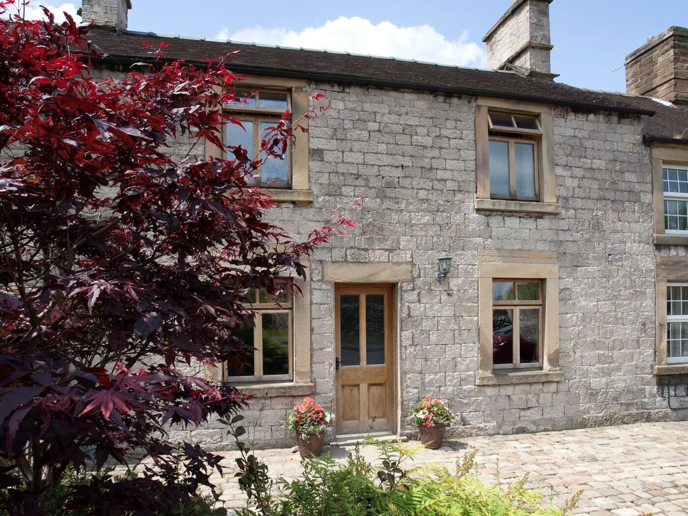 A stone building with a wooden door, two windows, and a small garden with potted plants.