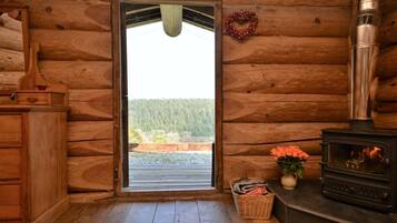 A log cabin interior with a wooden door, a fireplace, a wicker basket, and a vase with flowers.
