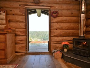 A log cabin interior with a wooden door, a fireplace, a wicker basket, and a vase with flowers.