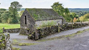 Ein Steinhaus mit geneigtem Dach, umgeben von einer Steinmauer und einem Kiesweg.