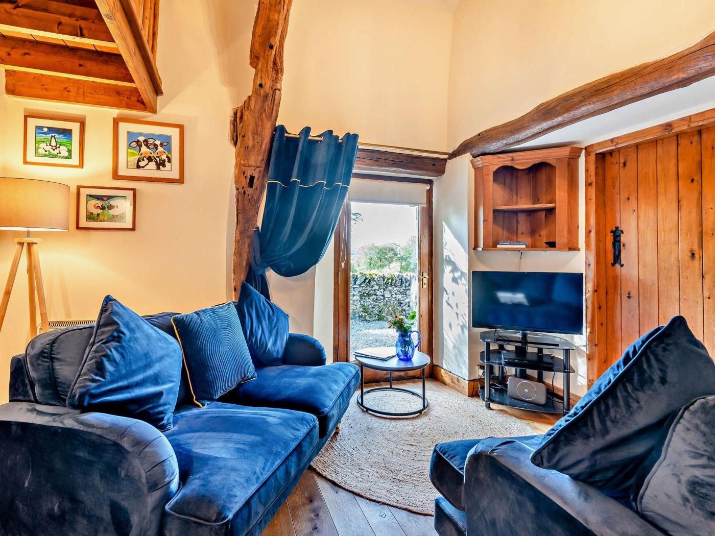 A cozy living room with a blue sofa, a television, and a rustic wooden ceiling.