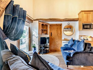 Ein gemütliches Wohnzimmer mit einer Couch, einem Fernseher und einer Küchenzeile mit Holzschränken und einer Mikrowelle.