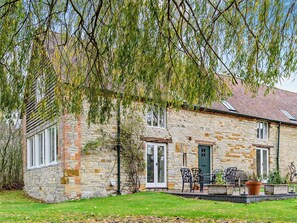 A stone building with a green door, a window with white shutters, and a patio with outdoor furniture. - 3 Bed in Stratford -upon- Avon (oc-54081) (Ettington)