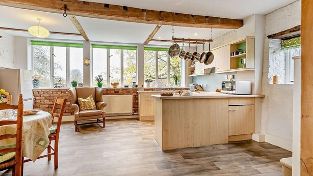 Eine moderne Küche mit Holzbalken, einem Essbereich mit Tisch und Stühlen sowie großen Fenstern mit Blick auf Bäume.