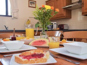 A breakfast table with a fruit bowl, a watermelon slice, a glass of orange juice, a glass of water, a vase with flowers, and a toaster. - 3 Bed in Tavistock (oc-54302) (Tavistock)