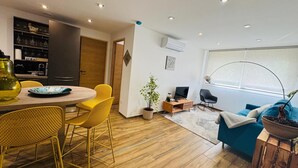 Een moderne woonkamer met een eethoek, houten vloeren en een groot raam met uitzicht.