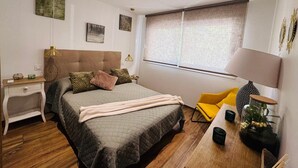 Een moderne slaapkamer met een groot bed, nachtkastjes, een bureau, een stoel, een raam met jaloezieën en een lamp.