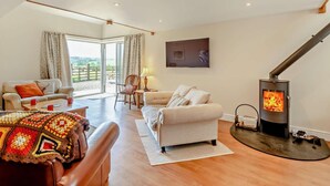 A spacious living room with a fireplace, a sofa, a chair, and a large window. - 4 Bed in Carnforth (oc-54457) (Burrow-with-Burrow)