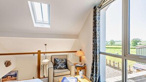 A bedroom with a bed, a desk with a lamp, a chair, a window with a view of the countryside, and a skylight. - 4 Bed in Carnforth (oc-54457) (Burrow-with-Burrow)