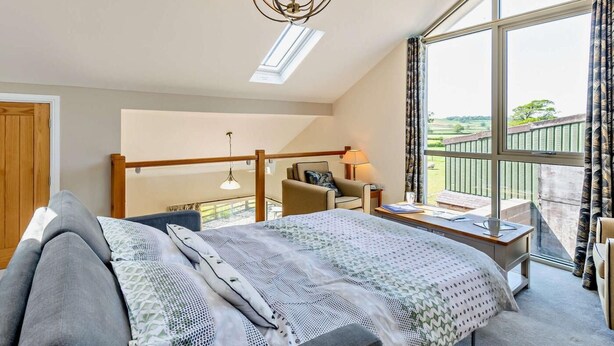 A bedroom with a bed, a desk, a chair, a balcony with a view, and a chandelier. - 4 Bed in Carnforth (oc-54457) (Burrow-with-Burrow)