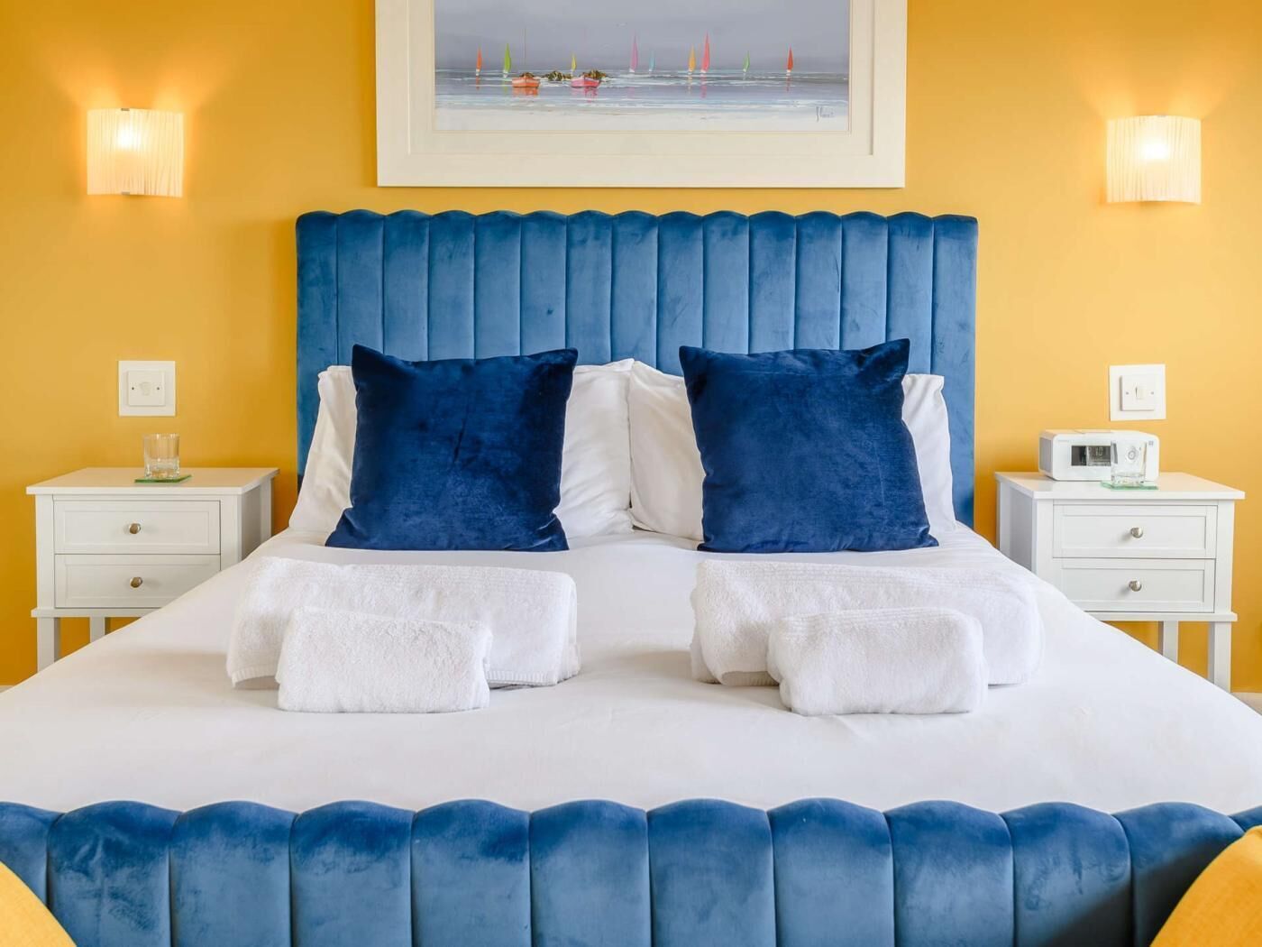 Una cama con cabecera tapizada en azul, ropa de cama blanca y dos almohadas a juego.
