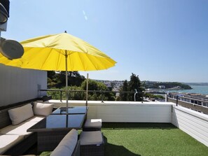 Un balcon avec un parasol jaune, des sièges d’extérieur et une vue sur la mer.