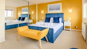 Habitación de hotel con una cama grande, una mesita de noche, una silla, un espejo y un cuadro en la pared.