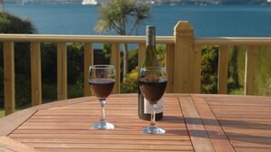 A wooden deck with two wine glasses and a bottle, overlooking a body of water and distant land. - 3 Bed in Brixham (oc-bx007) (Brixham)