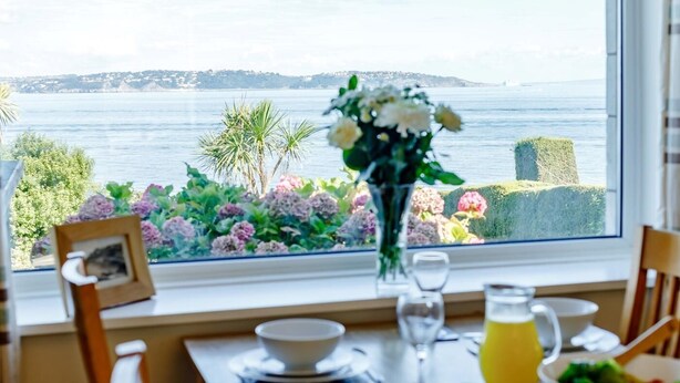 A dining table with a view of the sea, a vase with flowers, and a picture frame on the window sill. - 3 Bed in Brixham (oc-bx007) (Brixham)