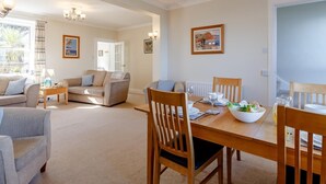 A spacious living area with a dining table, chairs, and a sofa. There are framed pictures on the walls and a chandelier. - 3 Bed in Brixham (oc-bx007) (Brixham)