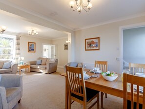 A spacious living area with a dining table, chairs, and a sofa. There are framed pictures on the walls and a chandelier. - 3 Bed in Brixham (oc-bx007) (Brixham)