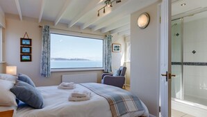 A bedroom with a large window, a bed with white linens, a chair, and a view of the sea. - 3 Bed in Brixham (oc-bx007) (Brixham)