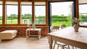 Una habitación con una mesa de madera, sillas, un banco y ventanas amplias con vista a la vegetación.