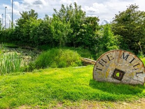 Ein großes, verrostetes Metallschild mit der Aufschrift 'THE MILE' in einer grünen Umgebung mit Bäumen und einem Gewässer im Hintergrund.