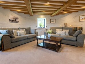 Ein Wohnzimmer mit zwei grauen Sofas, einem Holztisch und einem Fenster mit Blick auf Grünflächen.