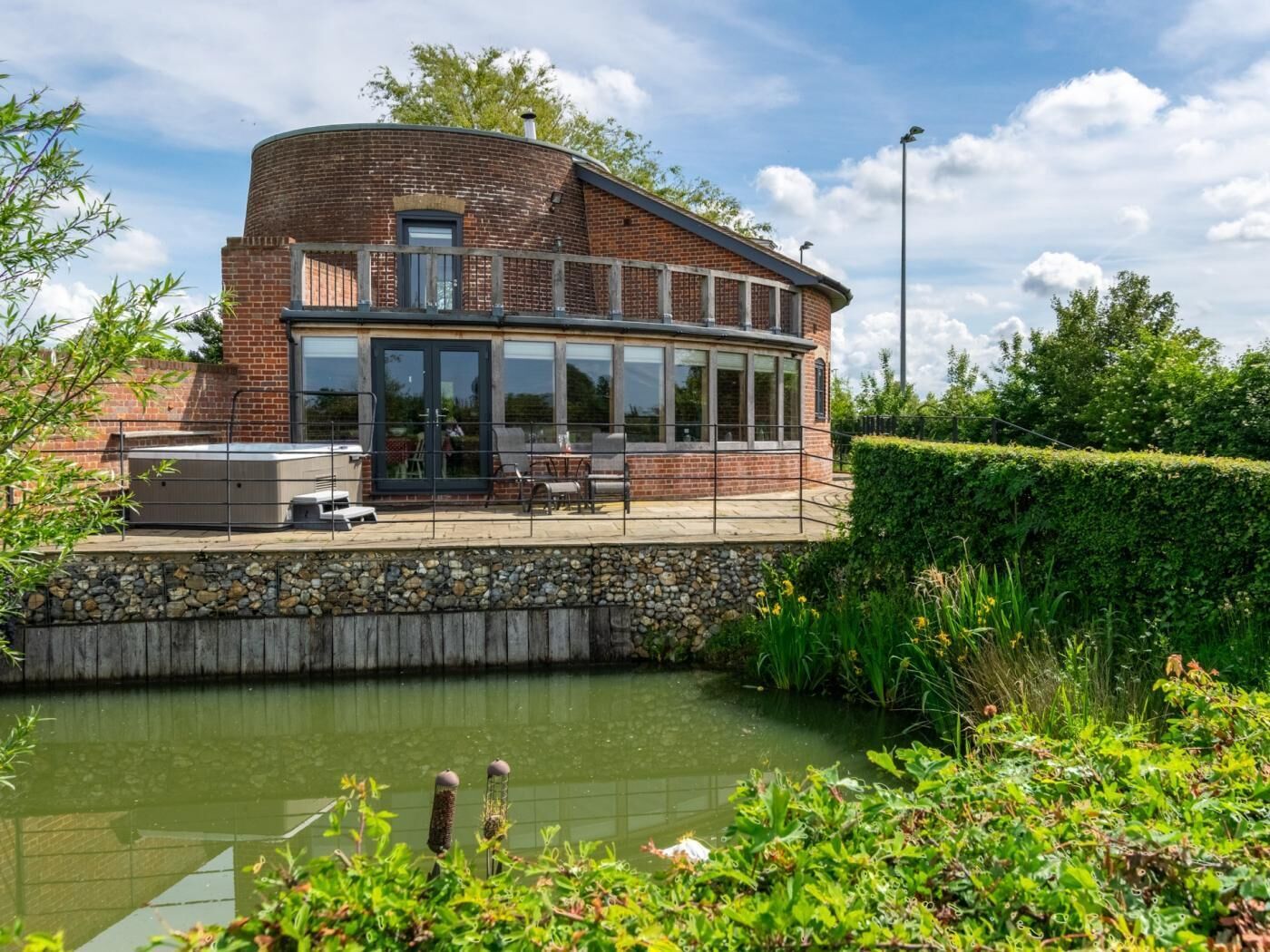 A brick building with a curved roof, a glass conservatory, outdoor seating, and a pond.