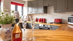 Una cocina moderna con armarios grises, una encimera de madera, un tostador rojo y una botella de vino.