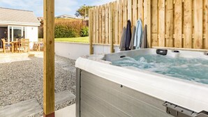 Un bain à remous sous une pergola en bois, avec vue sur un espace patio et une maison en arrière-plan.