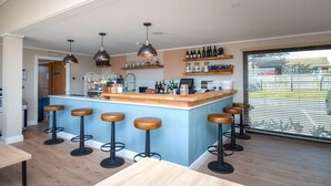 A modern kitchen with a bar area, wooden stools, pendant lighting, and a view through large windows.
