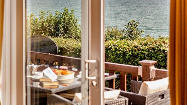 A balcony with a view of the sea, a grill, and outdoor furniture.