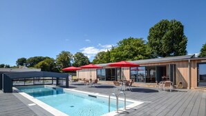 A swimming pool with a wooden deck, outdoor seating, and red umbrellas.