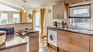 A compact kitchen with a washing machine, a sink, and a window with blinds.