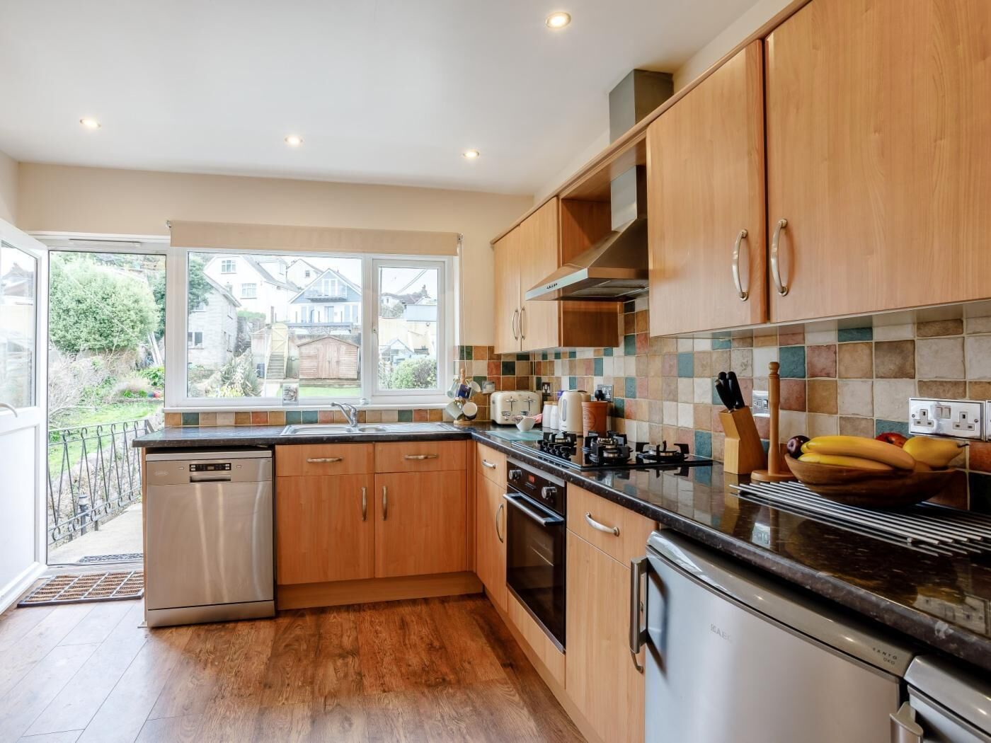 A modern kitchen with wooden cabinets, a stainless steel dishwasher, a built-in oven, and a tiled backsplash.