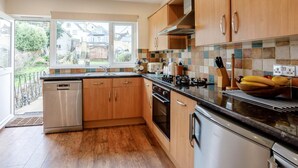 A modern kitchen with wooden cabinets, a stainless steel dishwasher, a built-in oven, and a tiled backsplash. - 3 Bed in Brixham (oc-bx001) (Brixham)