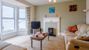 A living room with a television, fireplace, sofa, and large windows. - 3 Bed in Brixham (oc-bx001) (Brixham)