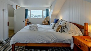 Quarto de hotel com cama, poltrona, mesa de cabeceira, luminária e janela com vista.