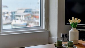 Quarto com janela vista para uma marina, uma televisão na parede e uma mesa com um vaso de tulipas e uma caneca verde.