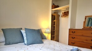 Ein ordentlich bezogenes Bett mit Kissen, ein Nachttisch mit Lampe, eine Holzkommode und ein gerahmtes Bild an der Wand.